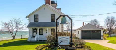 A white lighthouse with a bell, surrounded by a well-maintained lawn and a small building with a garage.