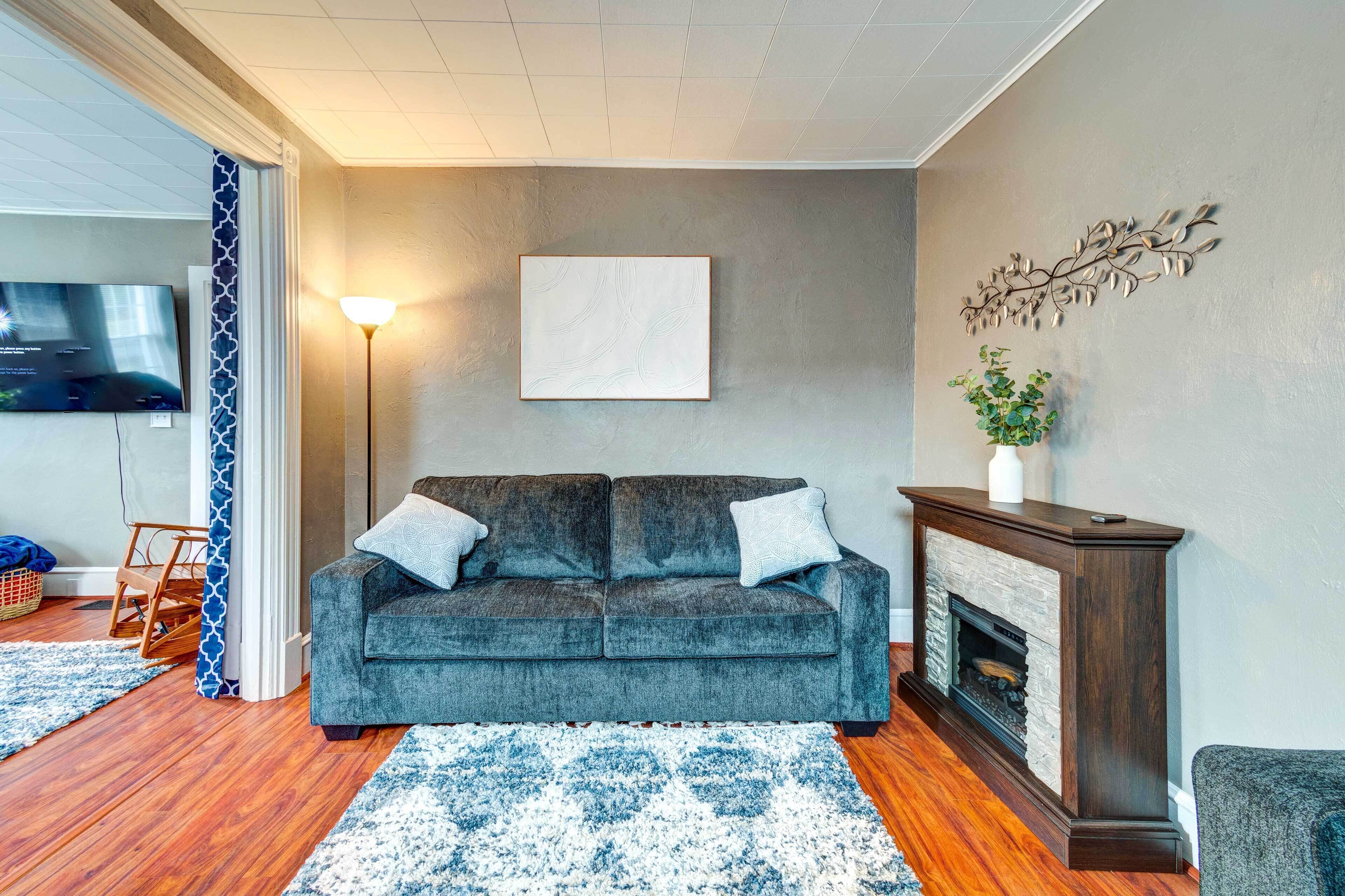 Un salon avec un canapé gris, une cheminée, un téléviseur et un tapis à motifs.