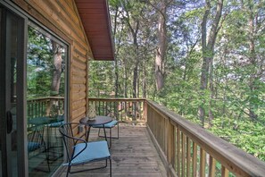 A wooden deck with two chairs and a table, surrounded by a wooden railing, overlooking a forested area.