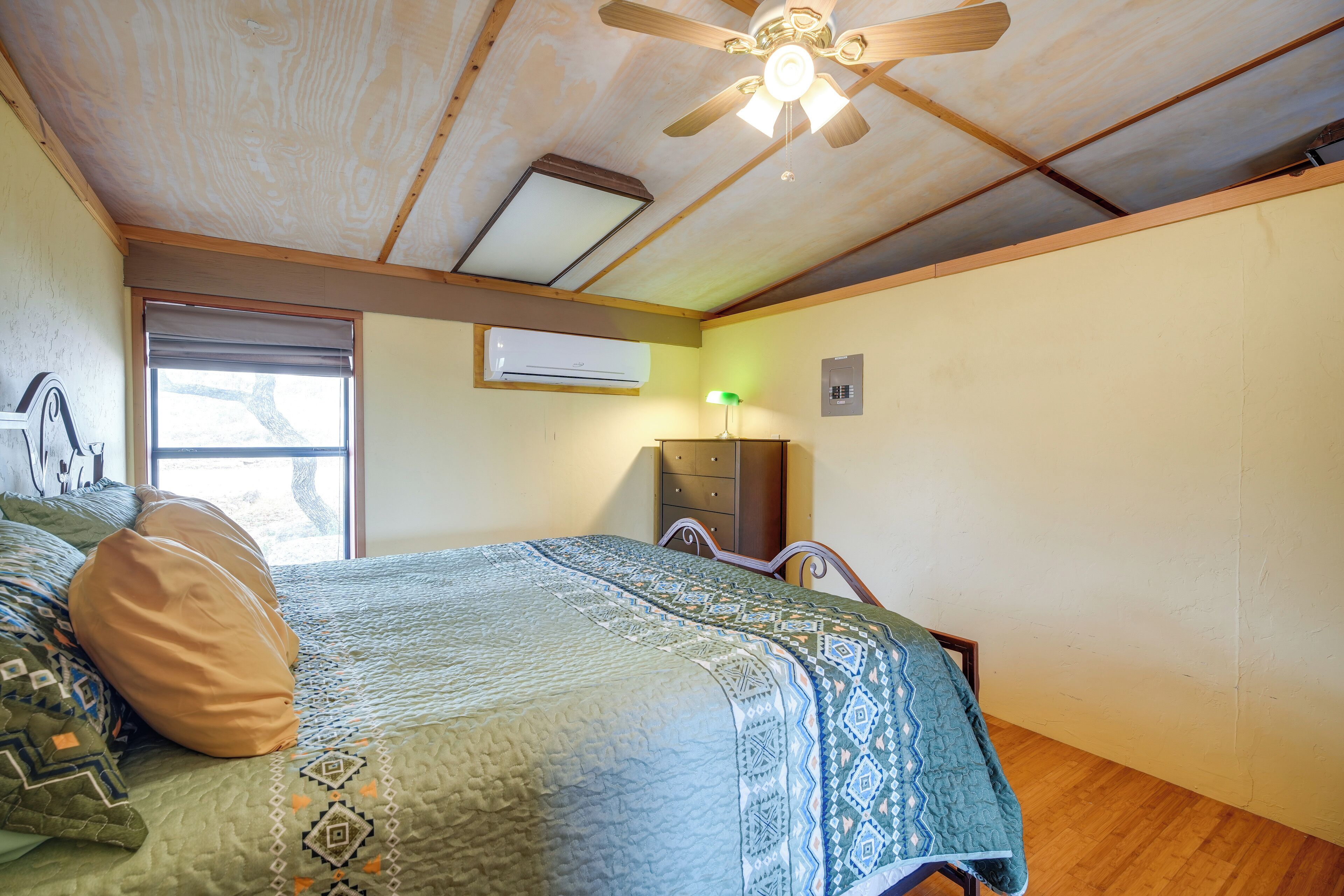 Een slaapkamer met een bed, een plafondventilator, een raam en een airconditioning.