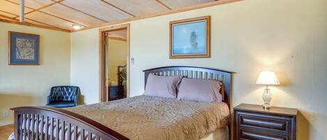 Un dormitorio con una cama de madera, una mesita de noche con lámpara, un cuadro enmarcado en la pared y una silla.