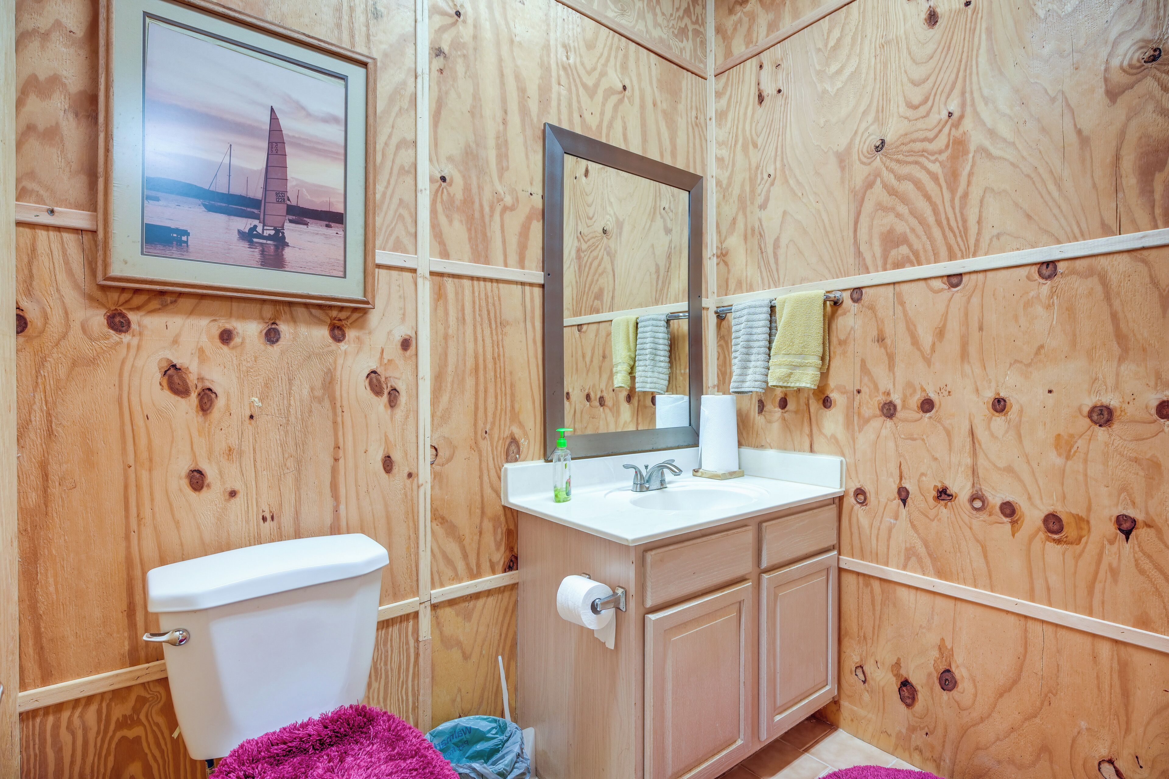 Een betegelde badkamer met toilet, wastafel, spiegel en een ingelijste foto aan de muur.