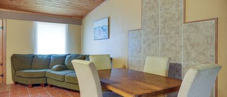 A cozy room with a wooden ceiling, a dining table with chairs, a green sofa, and a window with blinds.