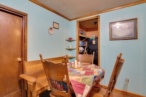 A dining area with a wooden table and chairs, a quilted tablecloth, and a kitchen in the background. - Serene Green Forest Hideaway w/ Spacious Yard (Green Forest)