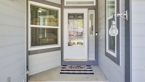 Puerta principal con una alfombra que dice 'hello', una ventana con persianas y un accesorio de luz en la pared.