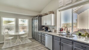 Una cocina moderna con armarios grises, encimera de granito y una zona de comedor con sillas blancas.