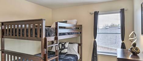 A bunk bed room with a window, a desk with a lamp, and a ceiling light.