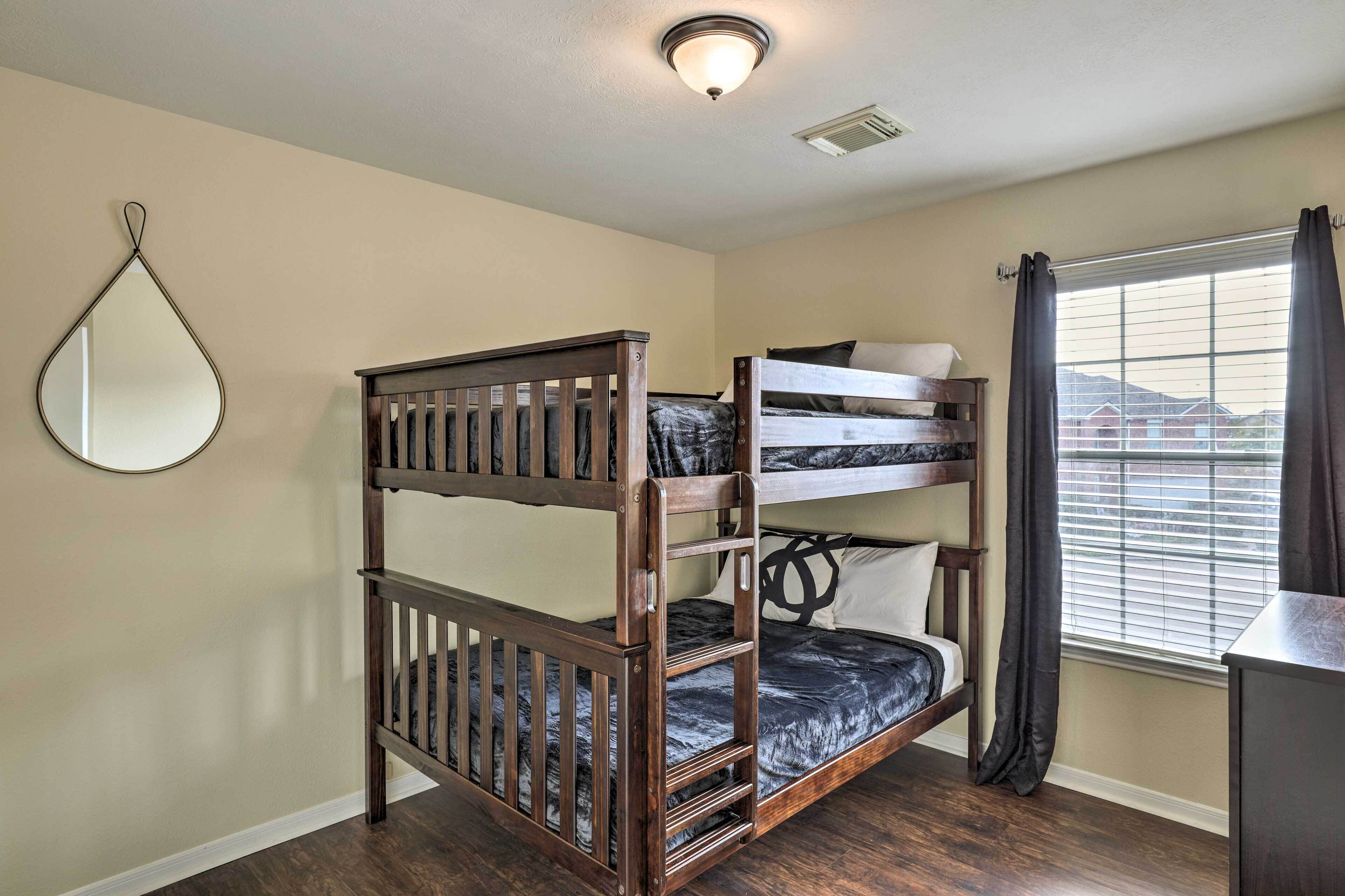 A bunk bed room with a wooden frame, a mirror on the wall, and a window with curtains.