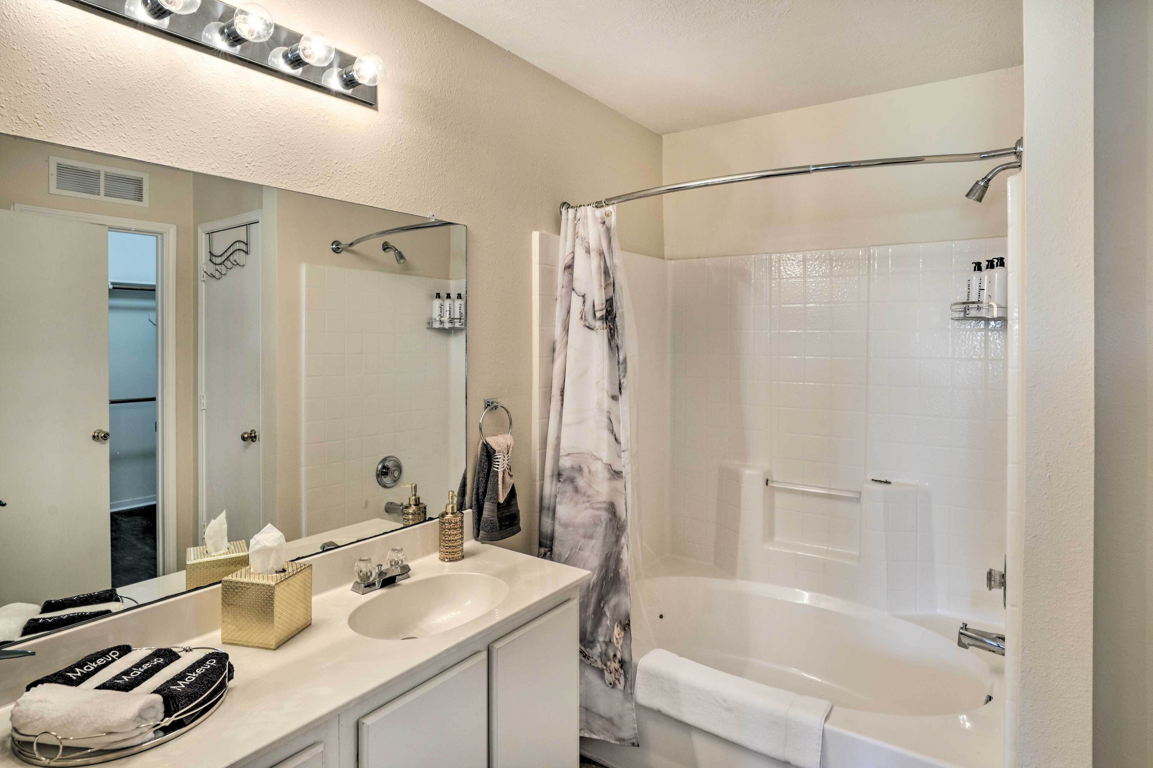 Une salle de bain avec un lavabo blanc, un miroir et une baignoire. On y trouve des serviettes et des articles de toilette sur le comptoir.