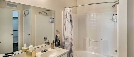 A bathroom with a white sink, mirror, and bathtub. There are towels and toiletries on the counter.