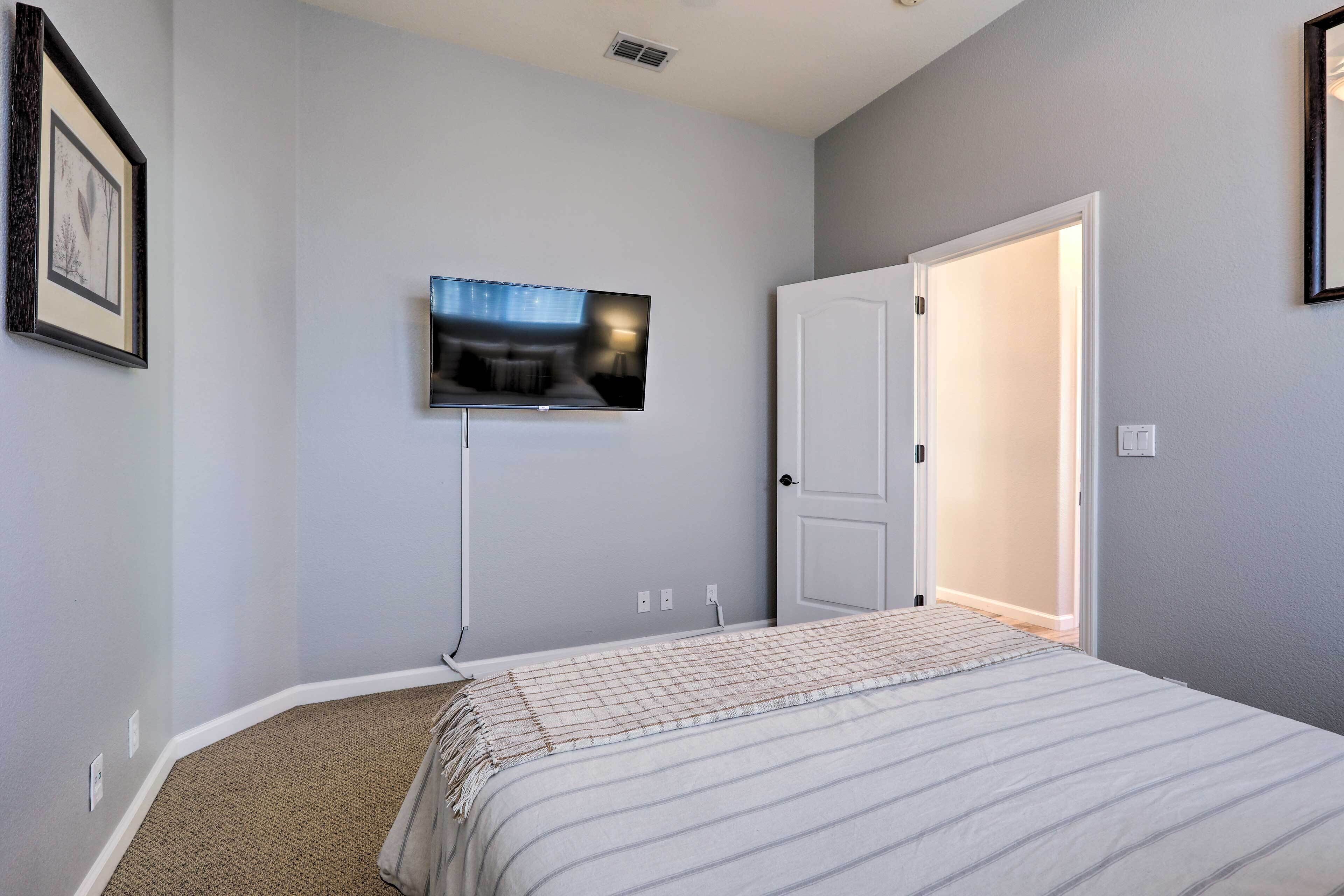 A bedroom with a bed, a television mounted on the wall, and a door leading to another room.
