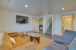 Una sala de estar con sofá, sillón y mesa de centro de vidrio. Una escalera conduce a otra habitación.