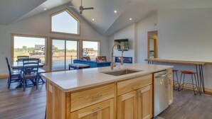 A spacious kitchen with a large island, wooden cabinets, and a dishwasher. There is a dining area with a table and chairs, and a blue sofa. - Lakefront Luxury - 1 MI to Buckhorn Boat Landing (New Lisbon)