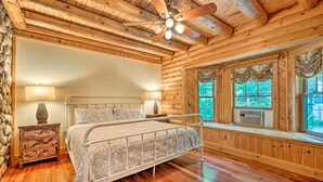A wooden cabin bedroom with a bed, nightstands, a ceiling fan, and large windows.