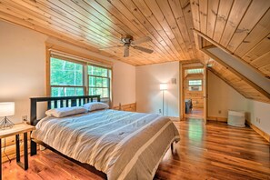 Ein Schlafzimmer mit Holzboden, einem Bett, einem Nachttisch, einem Fenster und einer Treppe.