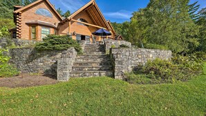 A log cabin with a stone staircase leading to the entrance, surrounded by lush greenery.