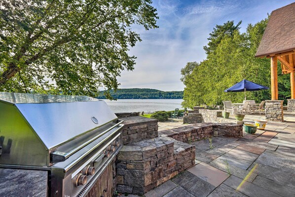 Eine Terrasse mit Grill, Steinmöbeln und Seeblick.