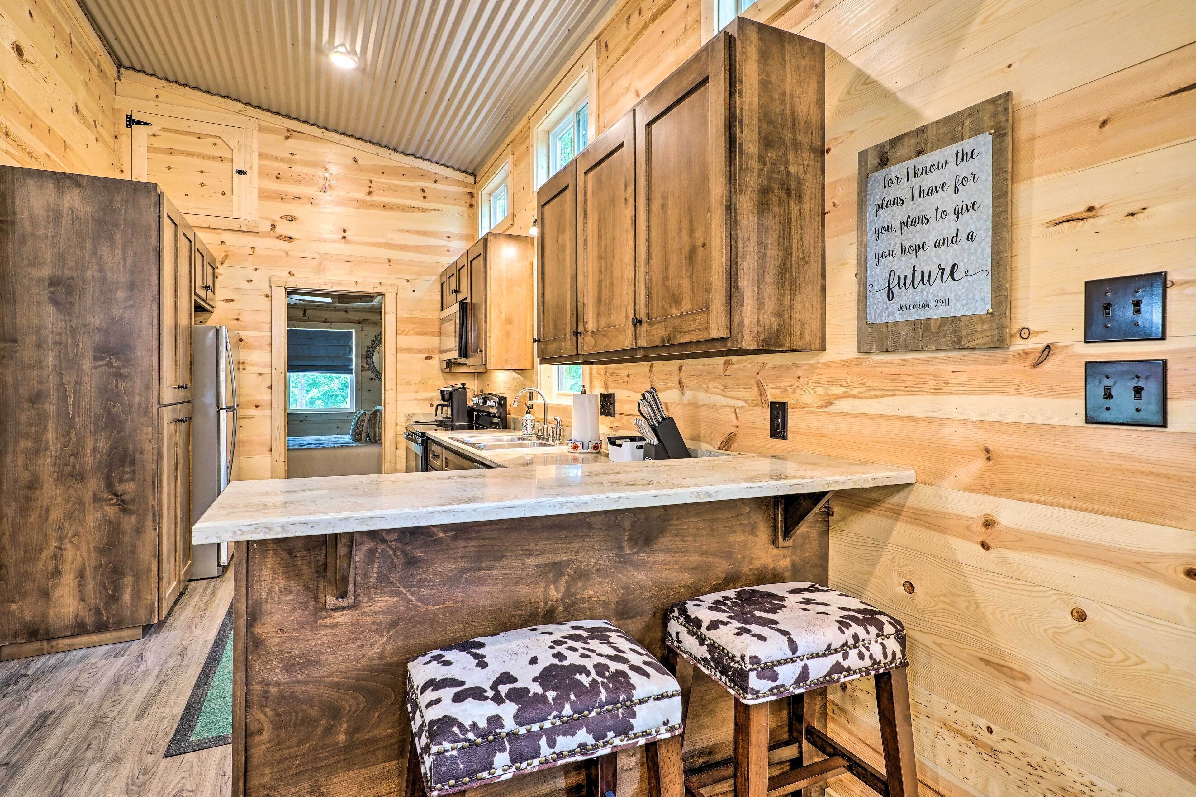 A wooden cabin interior with a kitchen area, wooden cabinets, a bar stool, and a motivational quote on the wall.
