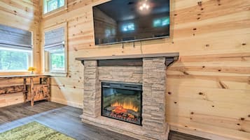 Une pièce chaleureuse avec une cheminée en pierre, des murs en bois et un grand téléviseur fixé au-dessus.