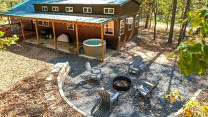 A covered outdoor area with a hot tub, fire pit, and Adirondack chairs. - Stylish Cabin by Beavers Bend: Hot Tub & Fire Pit (Broken Bow)
