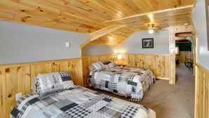 Una habitación acogedora con paredes y techo de madera, dos camas con ropa de cama a cuadros, una mesita de noche y una lámpara de pared.
