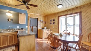 Interior de una cabaña de madera con cocina, comedor y un ventanal grande.