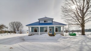 Una casa azul con un porche blanco y un camino de entrada cubierto de nieve.