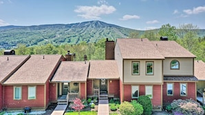 A two-story house with a red and beige exterior, a front porch, and a view of a mountain in the background. - Timber Creek Townhome w/ 2 Decks & Mtn Views! (West Dover)