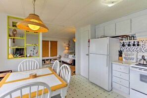 Een kleine keuken met witte kasten, een witte koelkast en een eethoek met een tafel en stoelen.