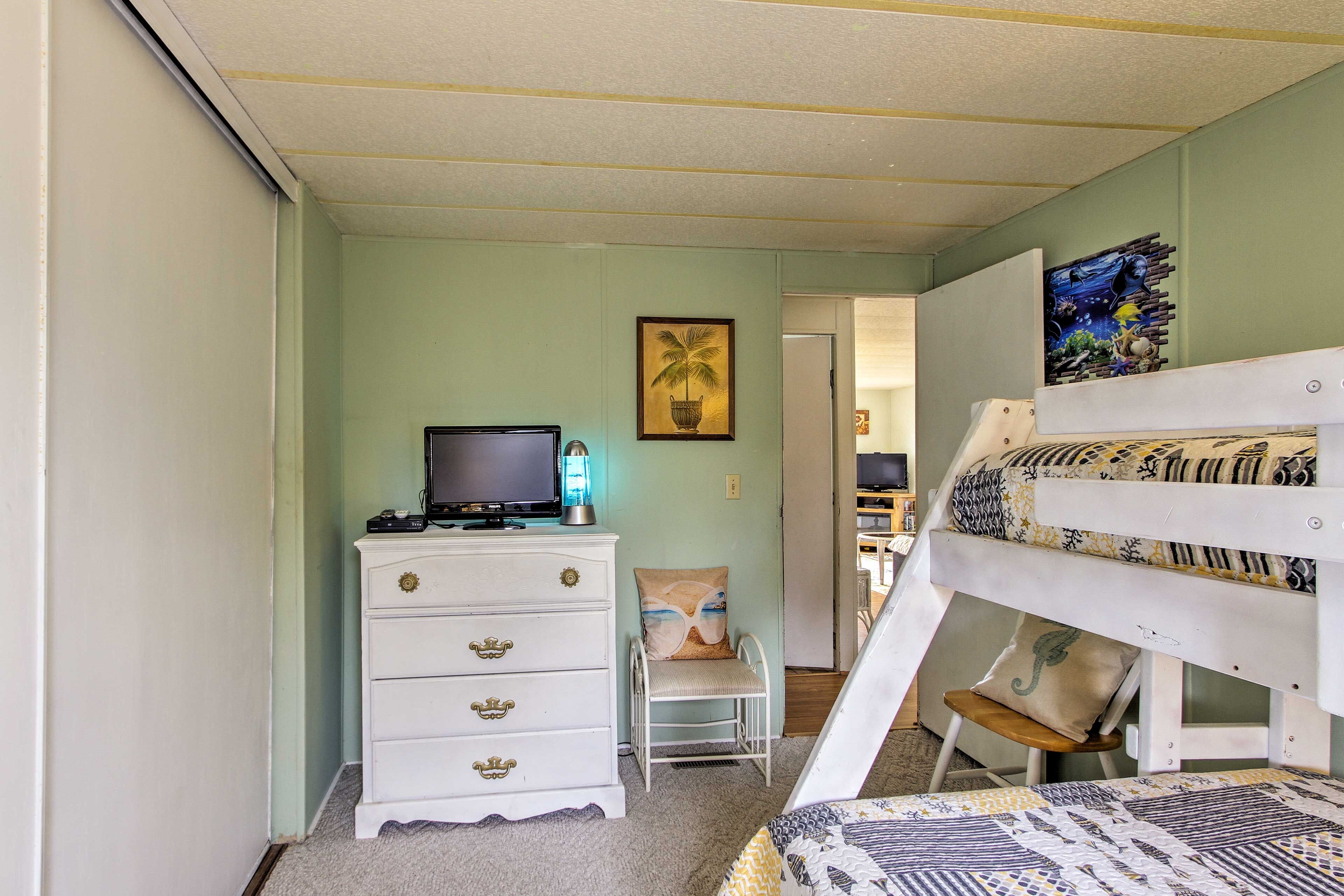 Een slaapkamer met een stapelbed, een dressoir met lades, een televisie op een standaard en een stoel.