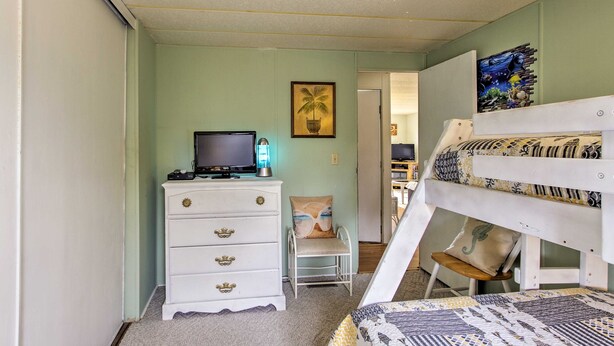 Un dormitorio con una cama litera, un aparador con cajones, un televisor sobre un mueble y una silla.
