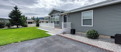 A single-story residential building with a front porch, a well-maintained lawn, and a gravel driveway.