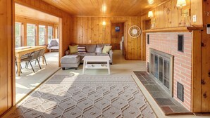 A cozy cabin interior with a fireplace, wooden walls, a sofa, and a dining area. - Waterfront Cottage w/ Sunroom + Patio & Grill (Clinton)