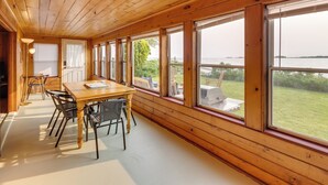 A wooden-paneled room with a large table and chairs, large windows, and a view of the outdoors. - Waterfront Cottage w/ Sunroom + Patio & Grill (Clinton)