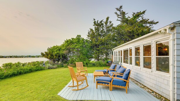 A deck with outdoor furniture, a grassy lawn, and a view of the water. - Waterfront Cottage w/ Sunroom + Patio & Grill (Clinton)