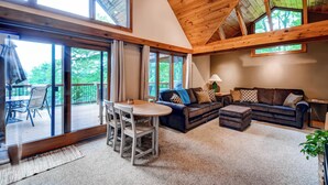 A spacious living area with a high ceiling, large windows, a dark-colored sofa, a small table, and a view of the outdoors. - Waterfront Highland Lake Home w/ Deck + Dock (Highland Lakes)