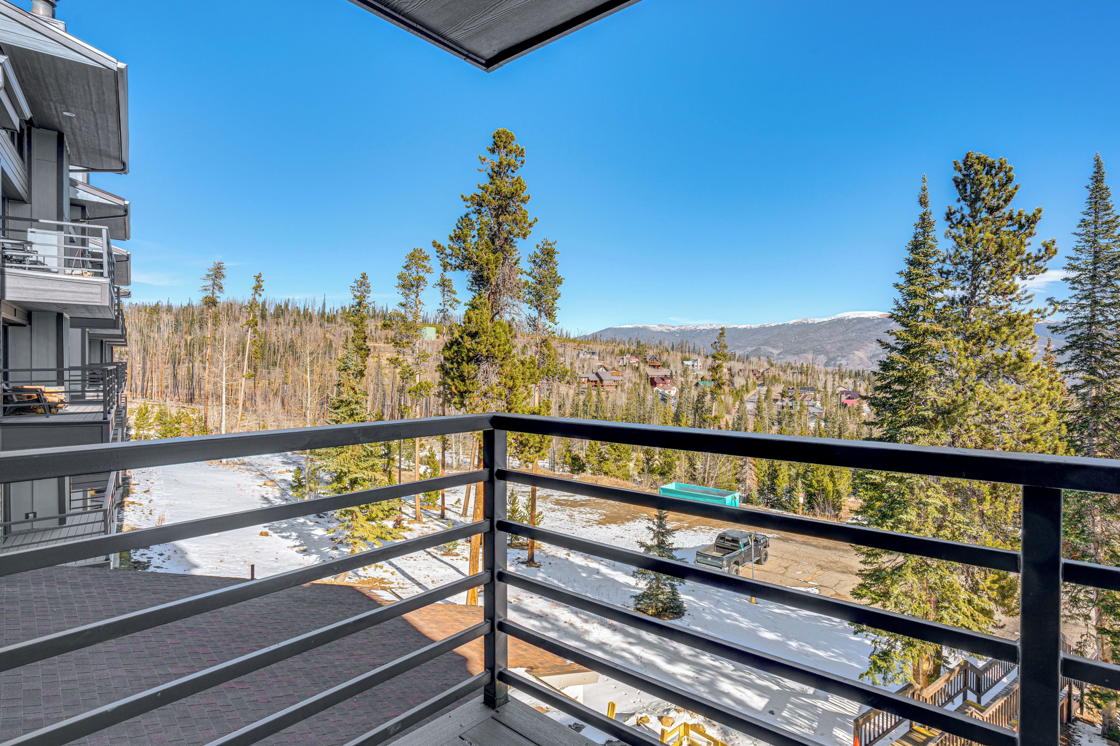 A balcony with a metal railing overlooking a snowy landscape, trees, and a distant mountain range.