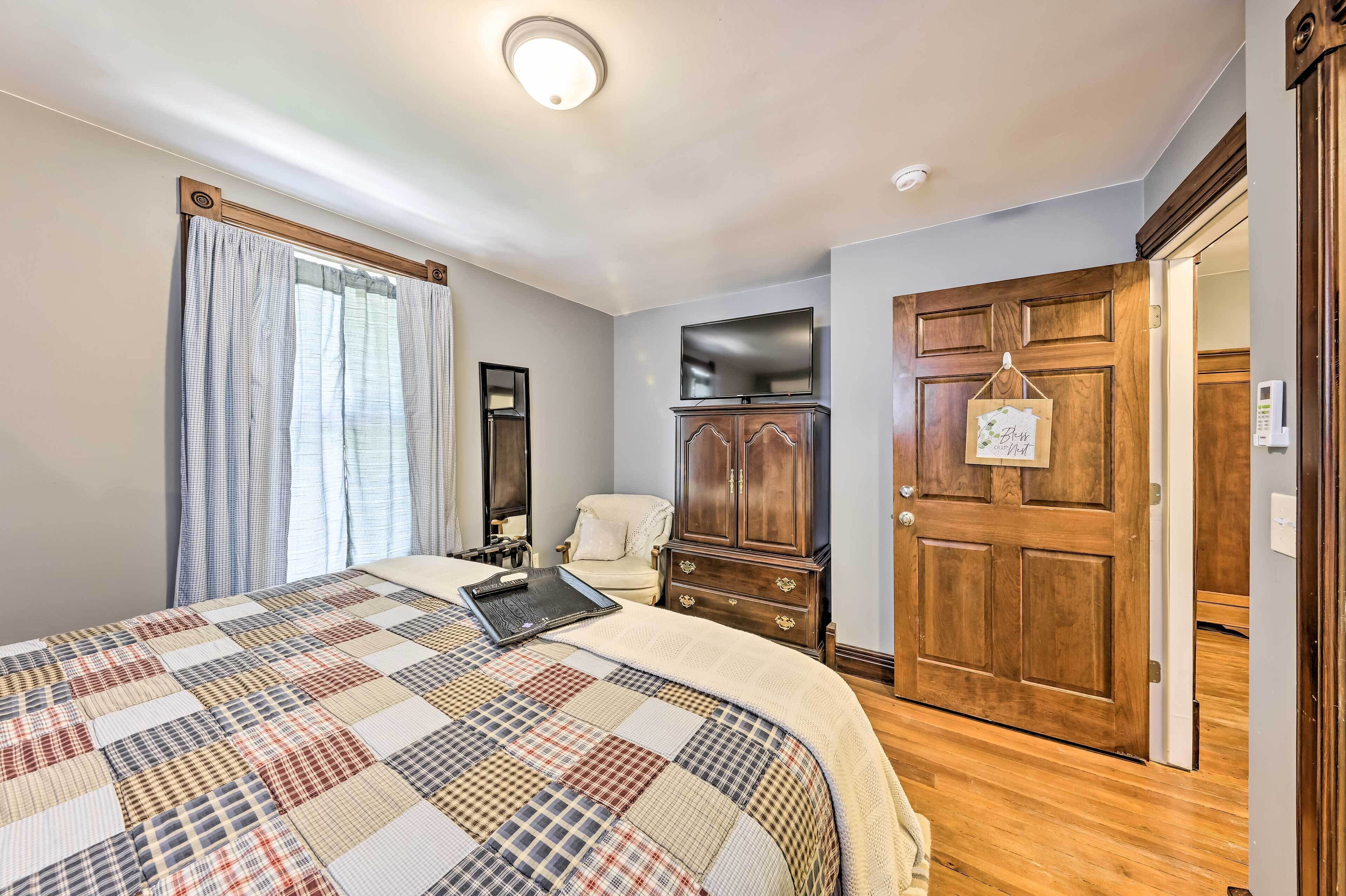Une chambre à coucher avec un grand lit, une armoire en bois, un téléviseur fixé au mur et une porte avec une pancarte.