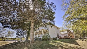 A two-story house with a porch, surrounded by trees and a grassy yard. - The Farmhouse at Deer Ridge Estate (Tonganoxie)