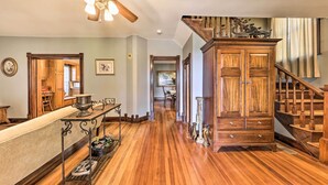 A spacious hallway with wooden flooring, a kitchen area with a wooden counter, and a staircase with a wooden railing. - The Farmhouse at Deer Ridge Estate (Tonganoxie)