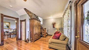 A spacious living room with hardwood floors, a wooden staircase, a sofa, and a dining area with a table and chairs. - The Farmhouse at Deer Ridge Estate (Tonganoxie)