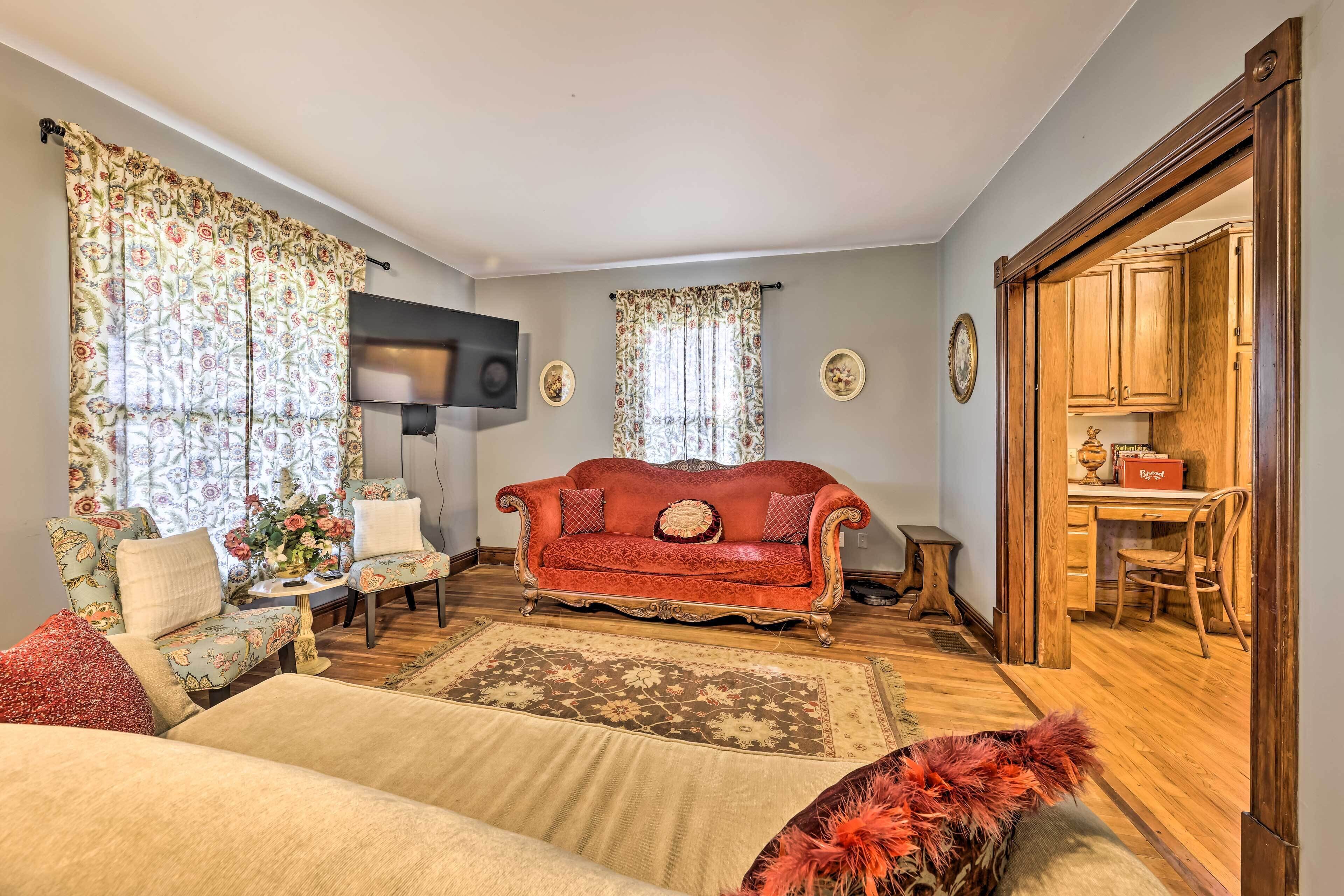 A living room with a red sofa, floral curtains, and a wooden dining area.