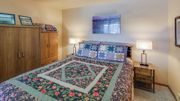 A bedroom with a bed, two bedside lamps, a wooden wardrobe, a framed picture on the wall, and a ceiling light. - Warm Mccall Condo: Half-mile to Payette Lake! (McCall)
