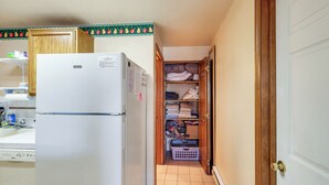 A compact kitchen with a refrigerator, a wooden cabinet, and a laundry basket in a narrow hallway. - Warm Mccall Condo: Half-mile to Payette Lake! (McCall)