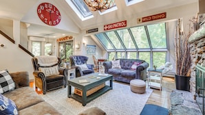 A spacious living room with a large clock, a ski patrol sign, and a wild thing sign. - Vermont Mountain Retreat: The Antler House (Plymouth)