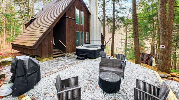 A cabin with a sloped roof, a hot tub, and wicker furniture in a forest setting. - Vermont Mountain Retreat: The Antler House (Plymouth)