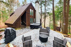 A cabin with a sloped roof, a hot tub, and wicker furniture in a forest setting. - Vermont Mountain Retreat: The Antler House (Plymouth)