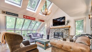 A spacious living room with a stone fireplace, large windows, and a high ceiling with skylights. - Vermont Mountain Retreat: The Antler House (Plymouth)