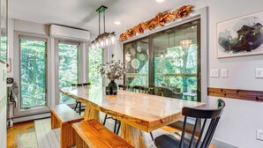 A modern kitchen with a large wooden table, benches, and a view of the forest through large windows. - Vermont Mountain Retreat: The Antler House (Plymouth)