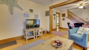 A living room with a television, a blue sofa, a wooden coffee table, and a staircase leading to another level. - Charming Urbana Home Near Downtown! (Urbana)